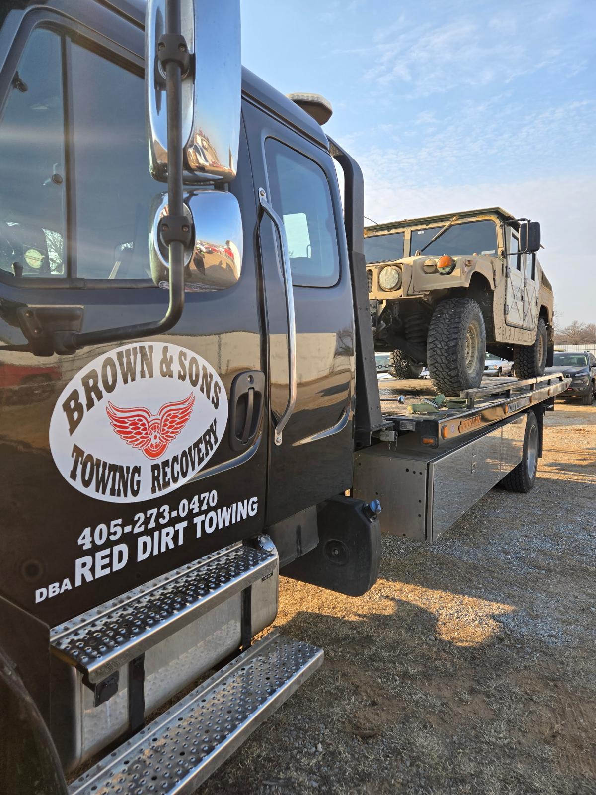 Brown & Sons black flatbed tow truck carrying a military Humvee