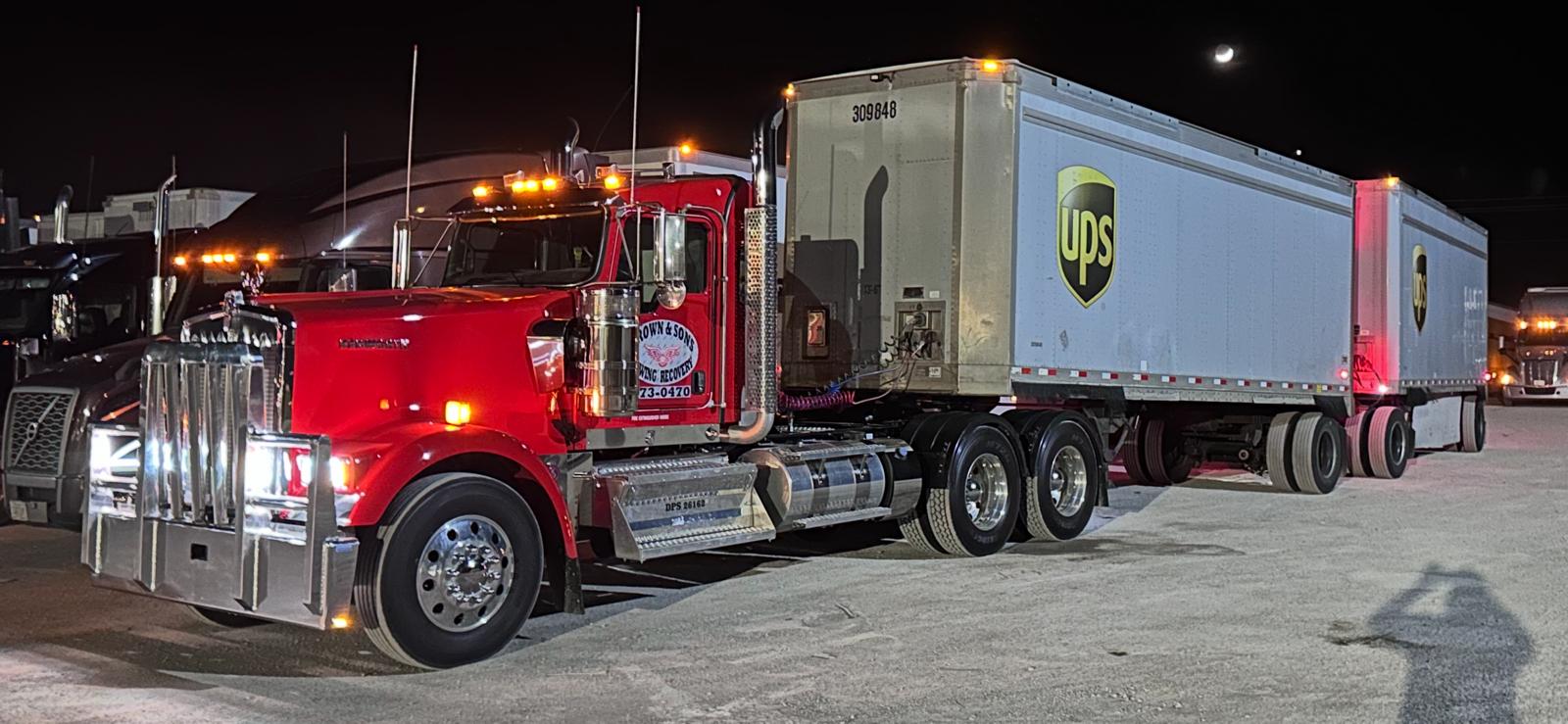 Brown & Sons heavy duty tow truck towing a UPS tractor-trailer at night